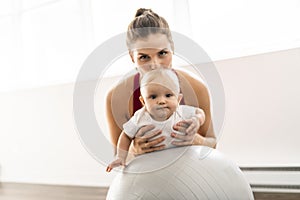 A Portrait of beautiful young mother in sports wear with her charming little baby in training session