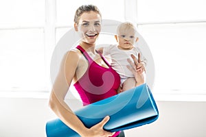 A Portrait of beautiful young mother in sports wear with her charming little baby in training session