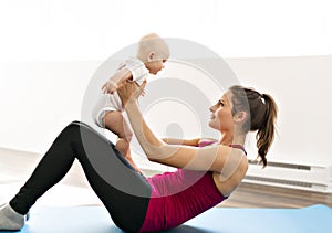 A Portrait of beautiful young mother in sports wear with her charming little baby in training session