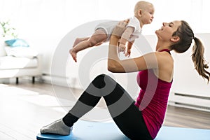 A Portrait of beautiful young mother in sports wear with her charming little baby in training session