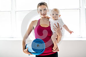 A Portrait of beautiful young mother in sports wear with her charming little baby in training session