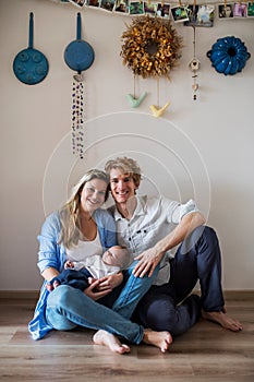 A portrait of beautiful young parents with a newborn baby at home.