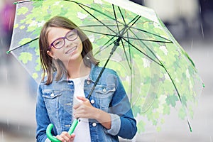 Portrait of beautiful young pre-teen girl with umbrella under spring or summer rain