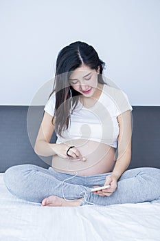 Portrait of Beautiful young pregnant woman putiing earphone on her tummy.Pregnancy health care preparing for baby concept.