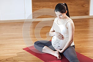 Portrait of a beautiful young pregnant woman sitting on yoga Mat On a wooden background