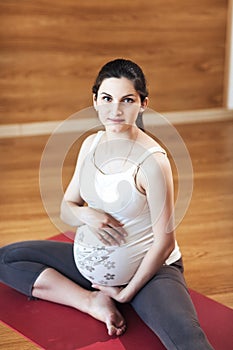 Portrait of a beautiful young pregnant woman sitting on yoga Mat On a wooden background