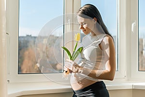Portrait of beautiful young pregnant woman with yellow tulip flower. Spring sunny day