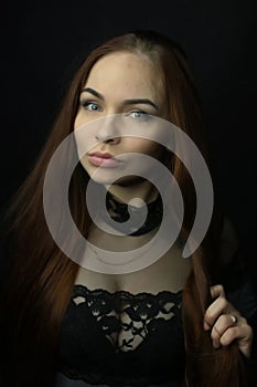 Portrait of a beautiful young red-haired girl on a dark black background in the studio, with a cleavage and big breasts in black