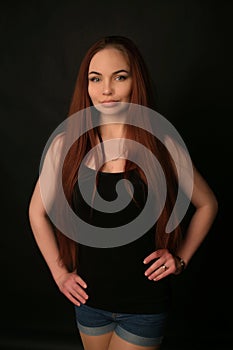 Portrait of a beautiful young red-haired girl on a dark black background in the studio, with a cleavage and big breasts in black