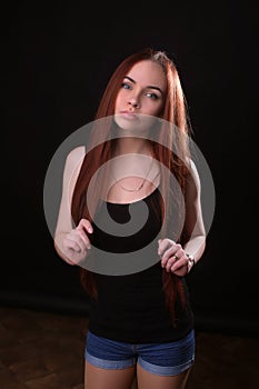 Portrait of a beautiful young red-haired girl on a dark black background in the studio, with a cleavage and big breasts in black