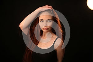 Portrait of a beautiful young red-haired girl on a dark black background in the studio, with a cleavage and big breasts in black