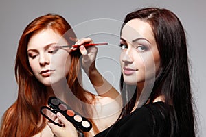 Portrait of beautiful young redheaded woman with esthetician making makeup