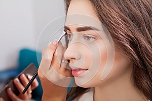 Portrait of beautiful young redheaded woman with esthetician making makeup eye shadow