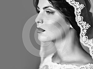 Portrait of beautiful young sensual bride in white lace dress and veil on head looking away.