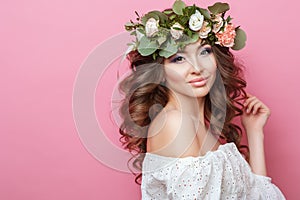 Portrait of beautiful young sexual sensual woman with perfect skin make up curly hair and flowers on head on pink background. Wrea