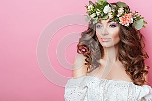 Portrait of beautiful young sexual sensual woman with perfect skin make up curly hair and flowers on head on pink background. Wrea
