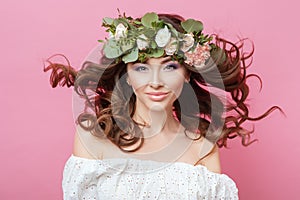 Portrait of beautiful young sexual sensual woman with perfect skin make up streaming hair and flowers on head on pink background.