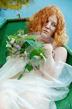 Portrait of beautiful young sexy redhead girl with a sad longing and a bouquet of wilted flowers in a boat