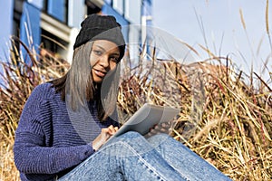 Portrait of a beautiful young smiling african woman using tablet pc computer sitting in the city in a sunny day