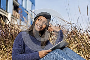 Portrait of a beautiful young smiling african woman using tablet pc computer sitting in the city in a sunny day