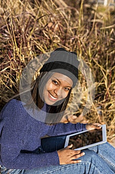 Portrait of a beautiful young smiling african woman using tablet pc computer sitting in the city in a sunny day