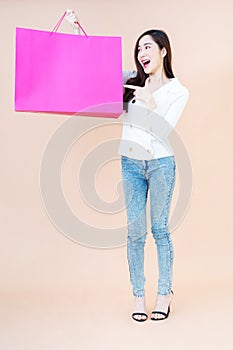 Portrait of Beautiful young smiling happy woman holding and finger pointing to shopping bags isolated orange background