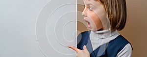 Portrait of beautiful young surprised girl looking behind white empty banner. Close up