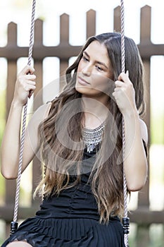 Portrait of beautiful young teenage girl in a dress while sitting on a wooden swing at the park