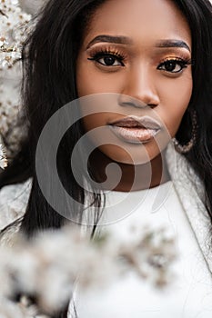 Portrait of a beautiful young tender woman near flowers on the street. Portrait of a cute african girl with clean black skin near