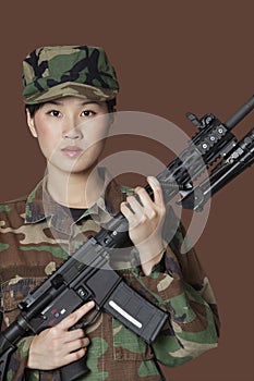 Portrait of beautiful young US Marine Corps soldier with M4 assault rifle over brown background