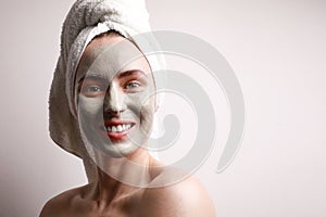 Portrait of beautiful young woman with applyed clay facial mask, wrap towel on head skin care treatment concept.
