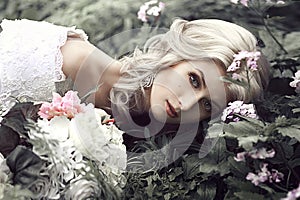 Portrait of a beautiful young woman as a princess lies in a forest with flowers.