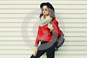 Portrait beautiful young woman with backpack posing wearing a red jacket, black round hat, scarf on white background