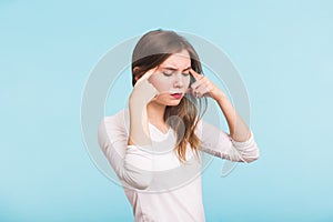 Portrait of beautiful young woman with bare shoulders touching her temples feeling stress, on blue background