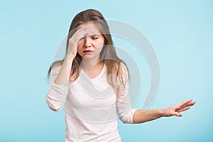 Portrait of beautiful young woman with bare shoulders touching her temples feeling stress, on blue background