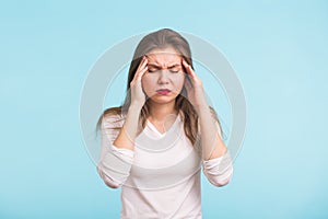 Portrait of beautiful young woman with bare shoulders touching her temples feeling stress, on blue background