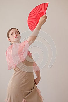 Portrait of a beautiful young woman in a beige and pink dress on a beige background. She is dancing flamenco. A hand with a red