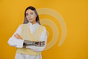 Portrait of a beautiful young woman with a bionic prosthetic arm in a white shirt on a yellow background.