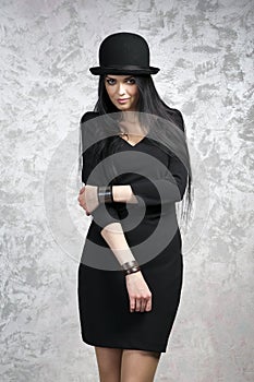 Portrait of a beautiful young woman in a black dress and bowler hat