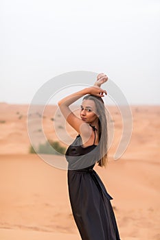 Portrait of beautiful young woman in black dress posing on sand in the desert