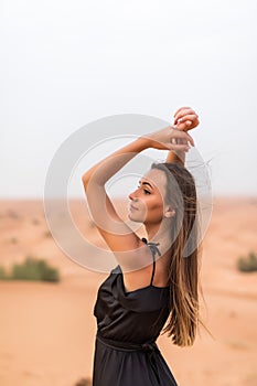 Portrait of beautiful young woman in black dress posing on sand in the desert