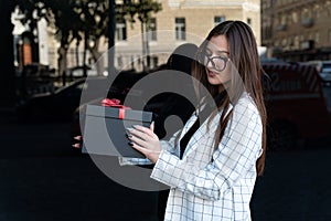 Portrait of beautiful young woman with black gift box in her hands. Happy stylish girl holds box with red bow
