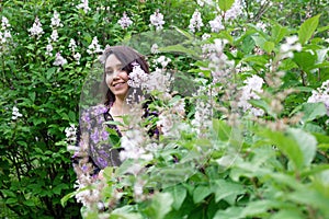 Portrait of beautiful young woman in black-purple dress in a garden with blooming lilac bushes