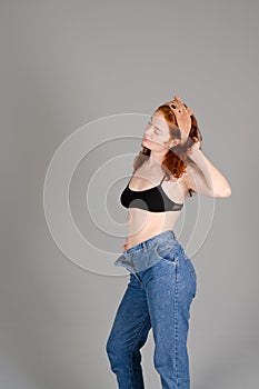 Portrait of beautiful young woman in black sports top and jeans with red curly hair, freckles and blue eyes