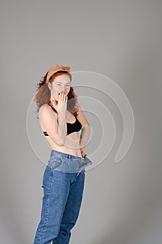 Portrait of beautiful young woman in black sports top and jeans with red curly hair, freckles and blue eyes