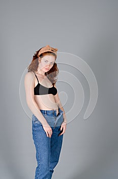 Portrait of beautiful young woman in black sports top and jeans with red curly hair, freckles and blue eyes