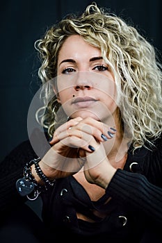 Portrait of a beautiful young woman with blond curly hair who with her fingers crossed looks intently in front of her