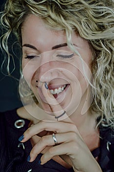 Portrait of a beautiful young woman with blond curly hair who with her index finger makes a sign of silence while smiling