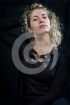 Portrait of a beautiful young woman with blond curly hair who holds her hair behind her neck with her hand and looks haughty