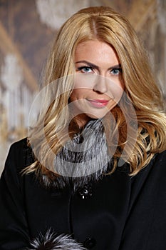 Portrait of beautiful young woman with blond hair wearing fashionable fur coat looking at camera.